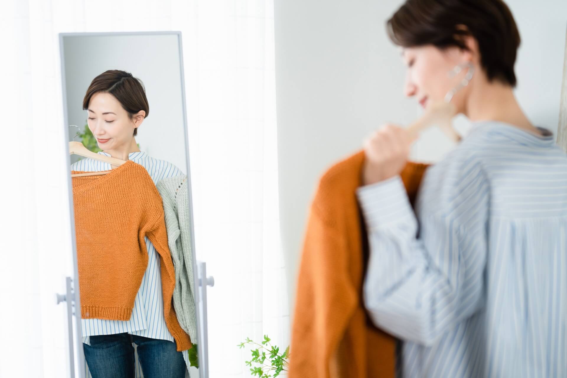 鏡の前でオレンジのニットを体に当てて似合うか確かめる女性