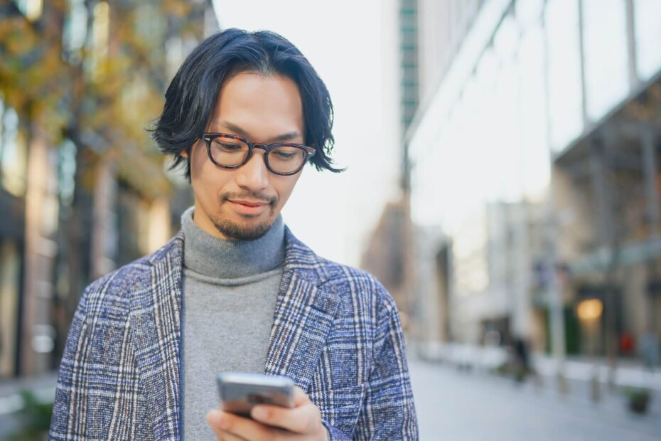 街中でスマートフォンを見ながら待ち合わせをするジャケット姿の男性