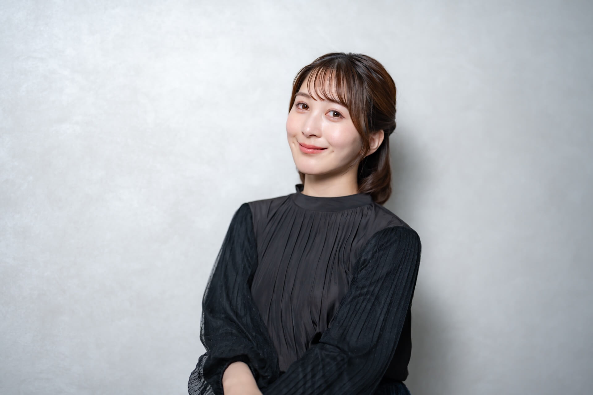 黒いブラウスを着てグレーの壁の前でほほえむ女性