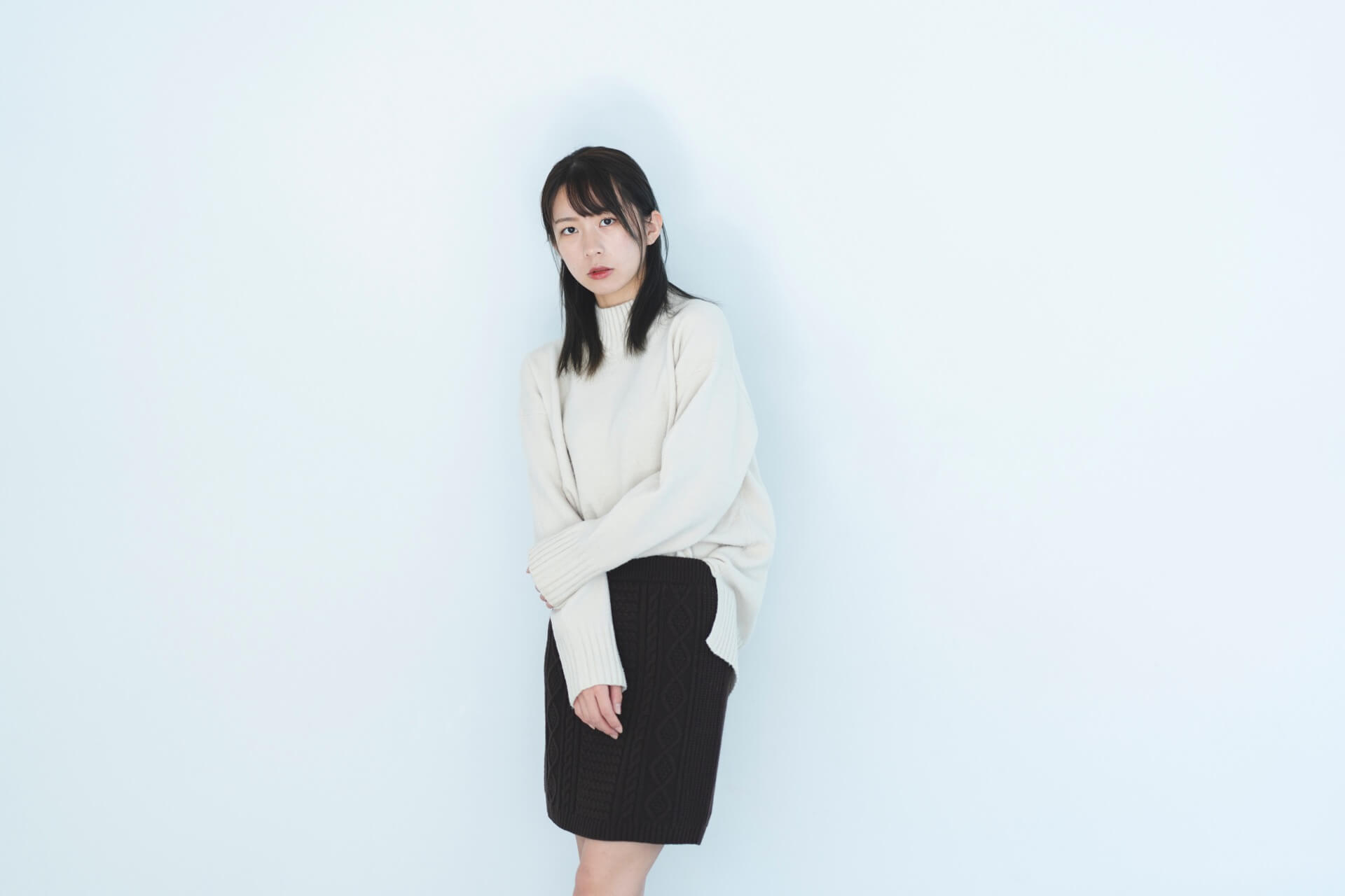 白いニットに黒いスカートを合わせて立つ女性