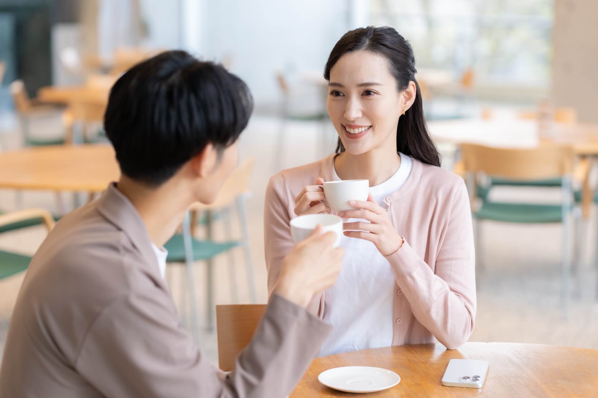 カフェのテーブルで向かい合い、カップを手に会話する日本人の男女