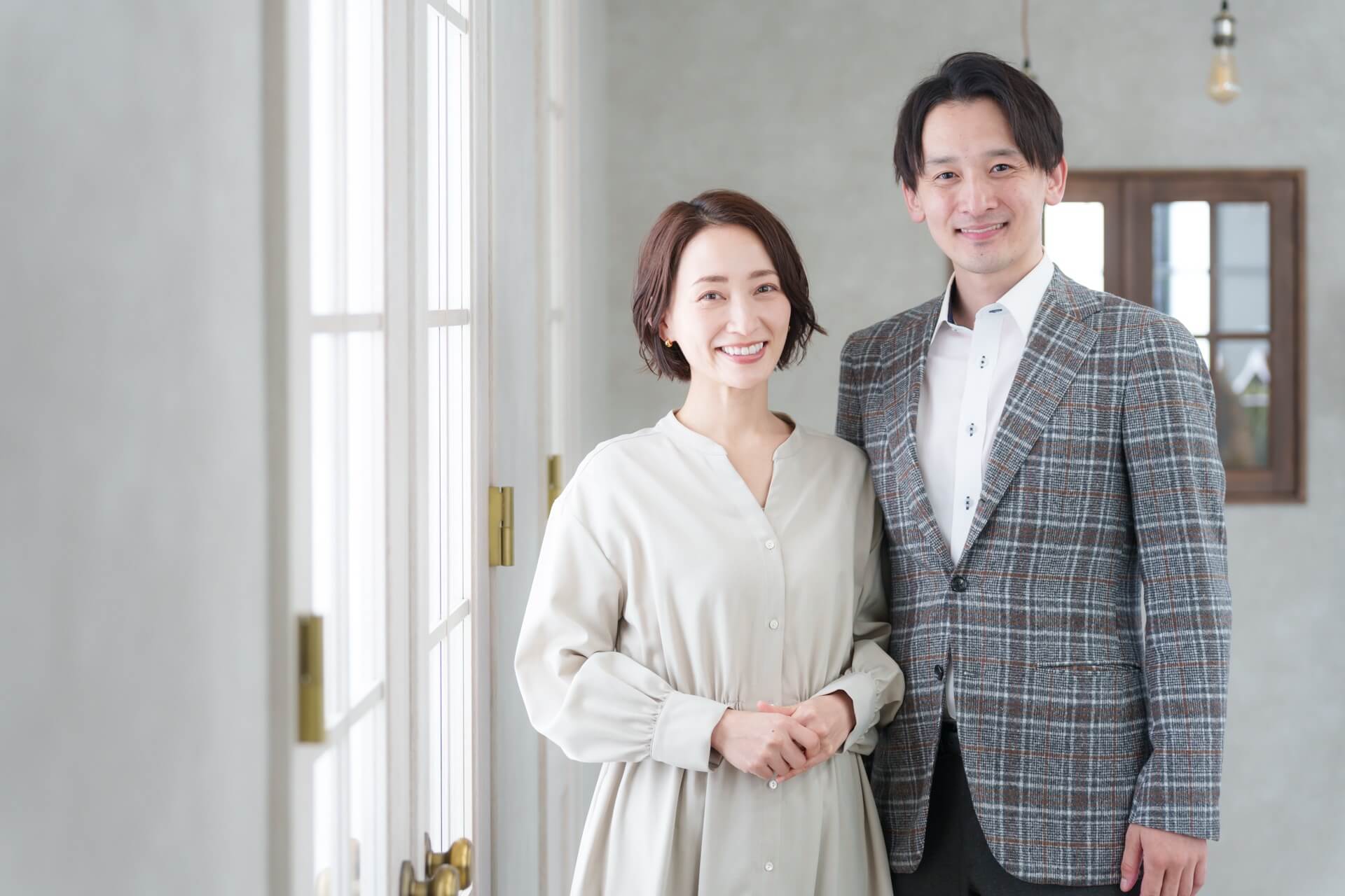 ジャケット姿の男性と、ベージュのワンピースを着た女性が並んで笑顔を見せる様子
