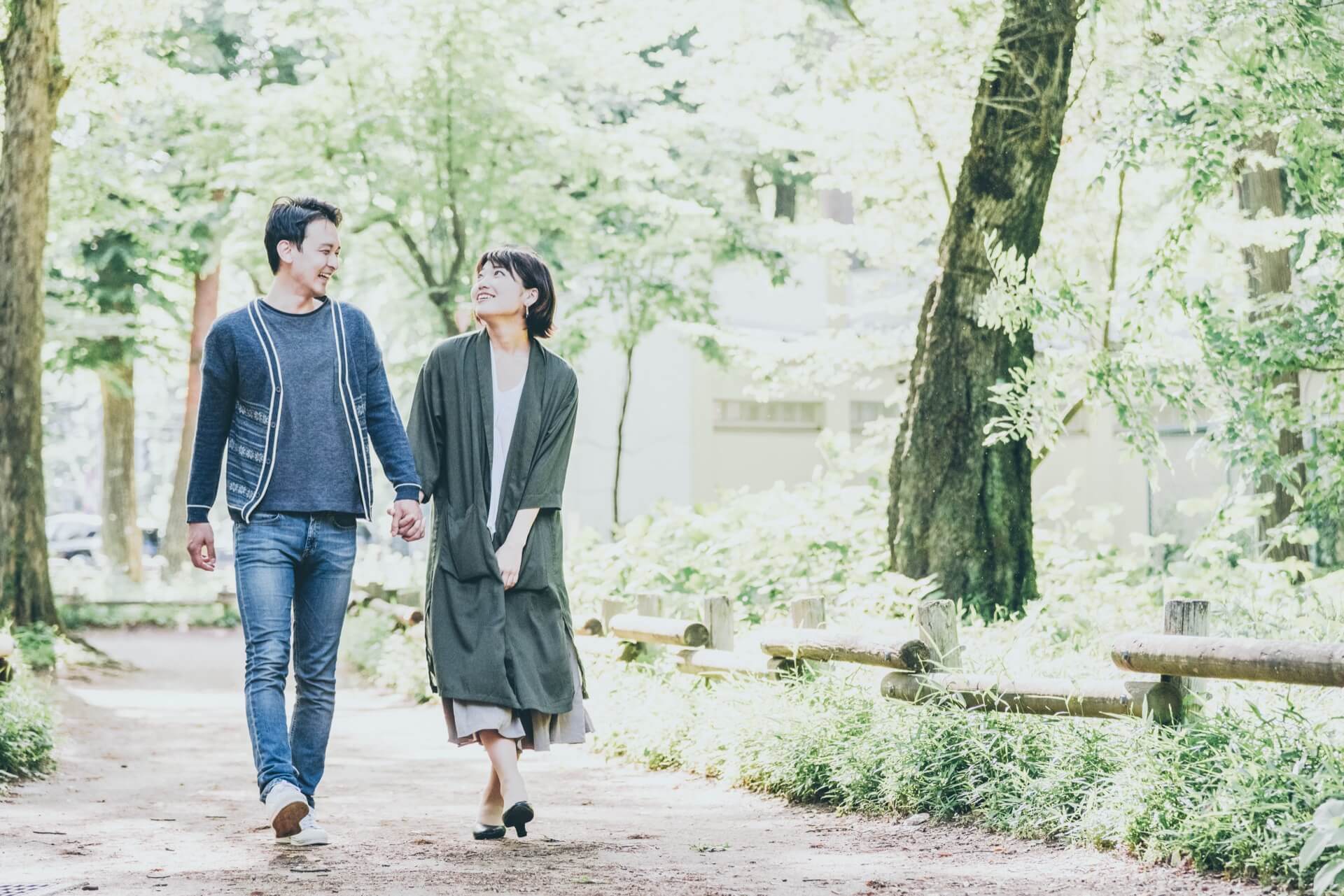緑の多い公園の小道を手をつないで歩く男女