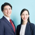ネイビーのスーツとジャケットをきちんと着こなし、笑顔で並ぶ日本人の男女