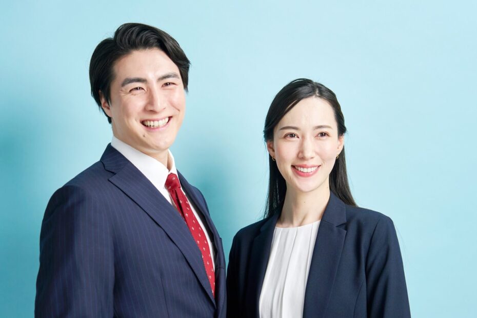 ネイビーのスーツとジャケットをきちんと着こなし、笑顔で並ぶ日本人の男女