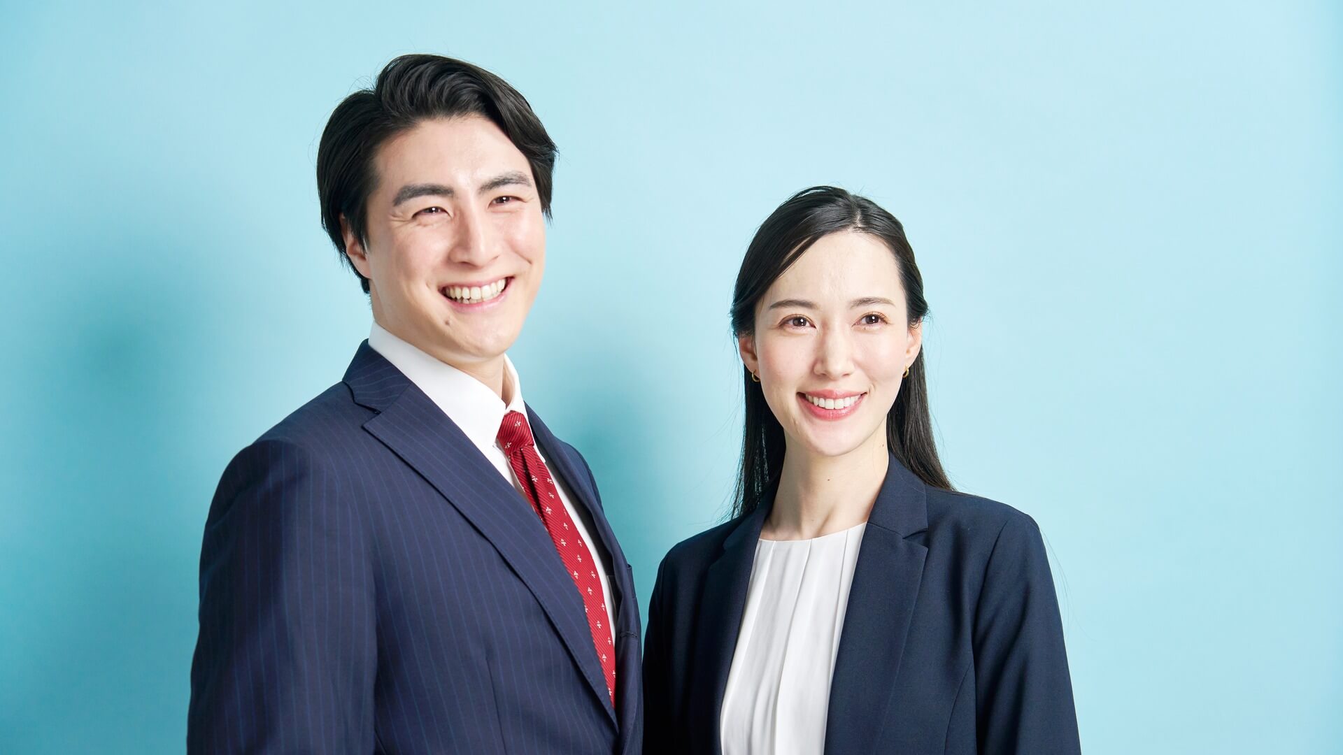 ネイビーのスーツとジャケットをきちんと着こなし、笑顔で並ぶ日本人の男女