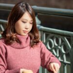 ピンクのタートルネックニットを着て、オープンカフェで食事をする女性