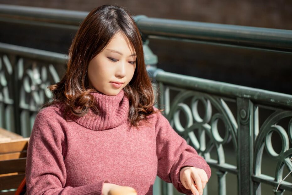 ピンクのタートルネックニットを着て、オープンカフェで食事をする女性
