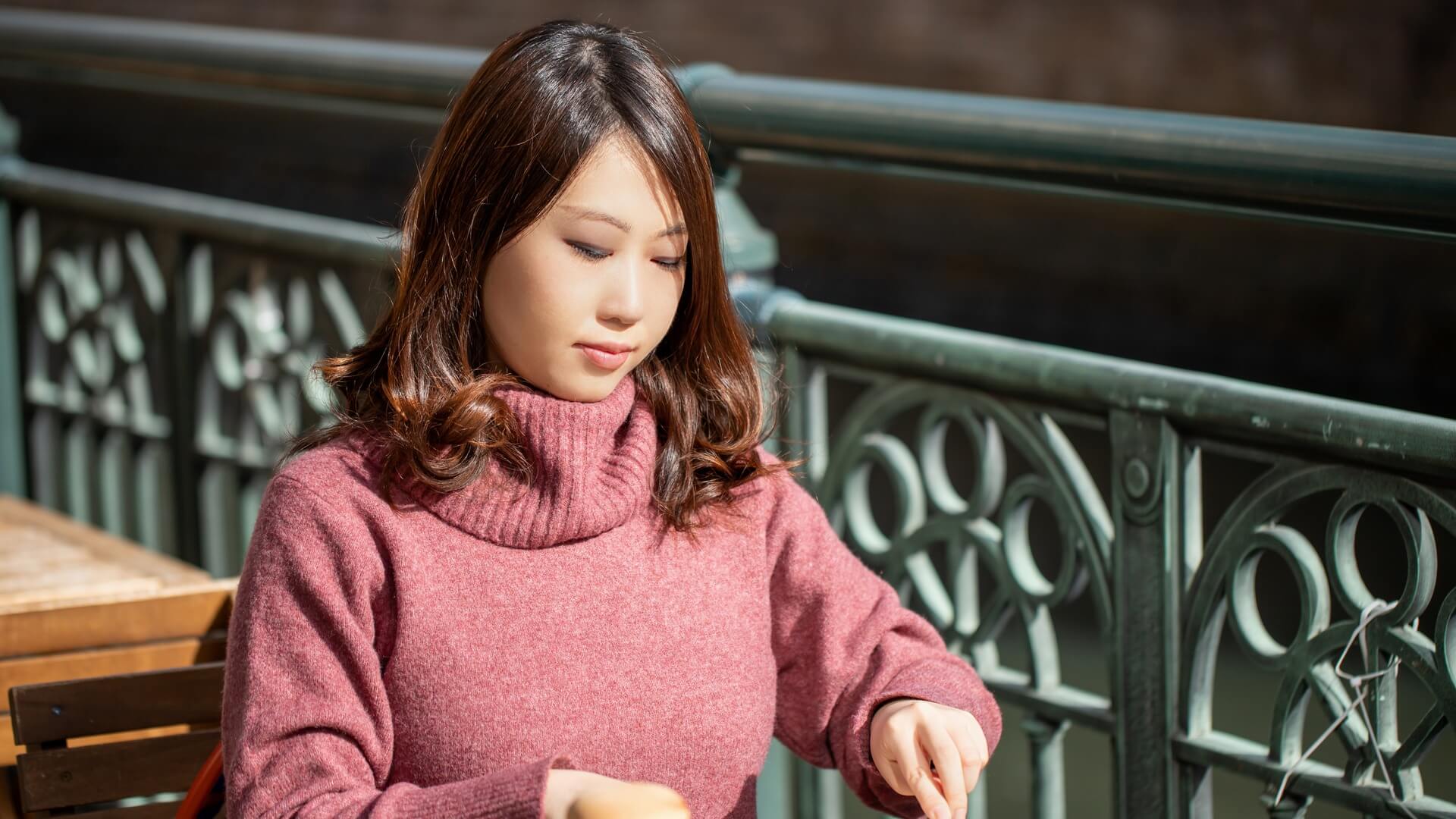 ピンクのタートルネックニットを着て、オープンカフェで食事をする女性