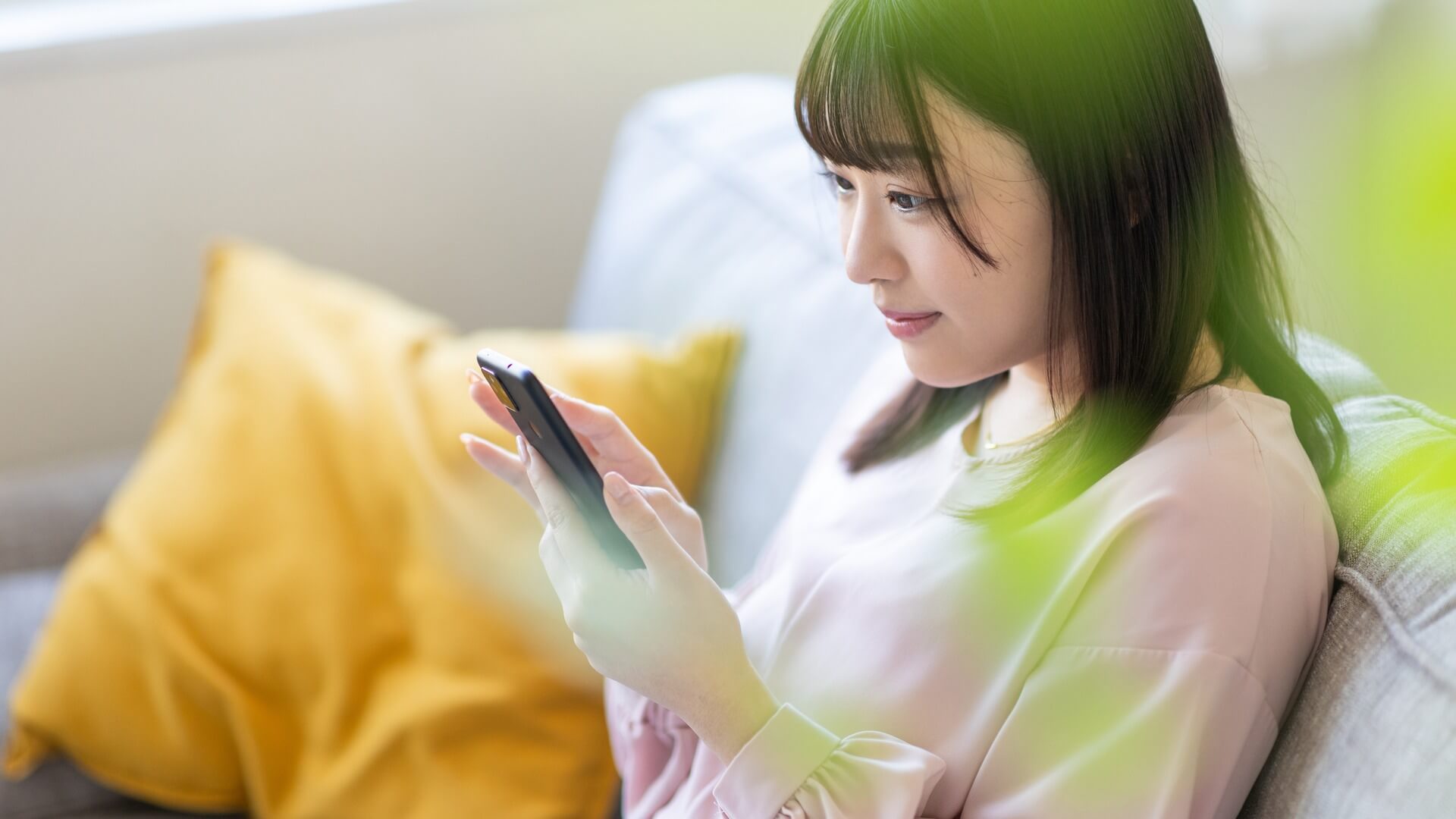 ソファでスマートフォンを操作する女性