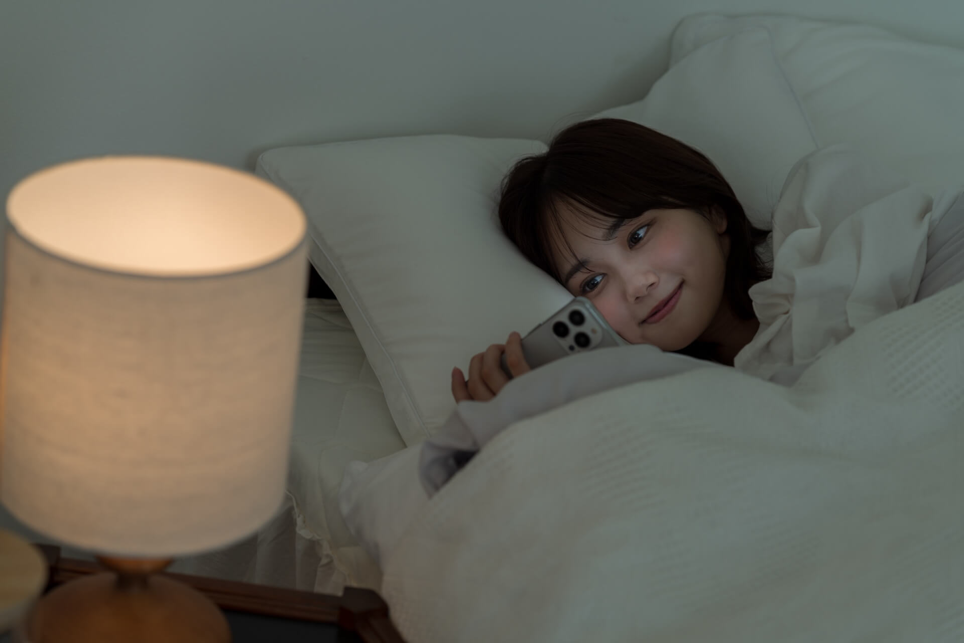 夜、ベッドの中でスマートフォンを見る女性
