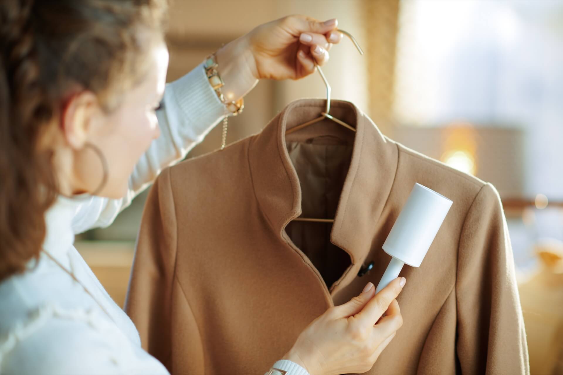 ハンガーに掛けたベージュのコートを粘着ローラーで手入れする女性