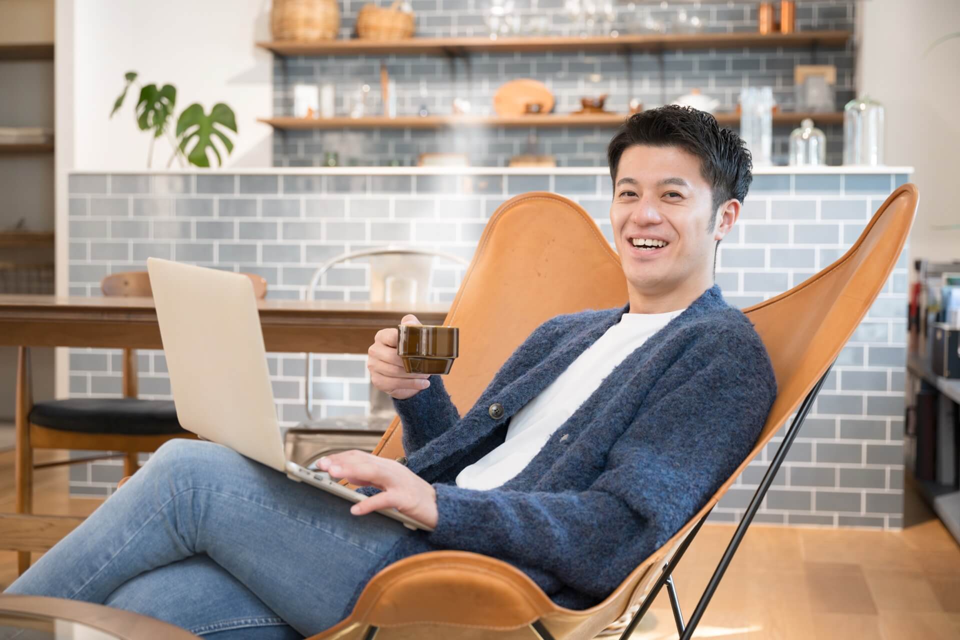 カーディガンを着てカフェの椅子に座り、コーヒーを手に笑う男性