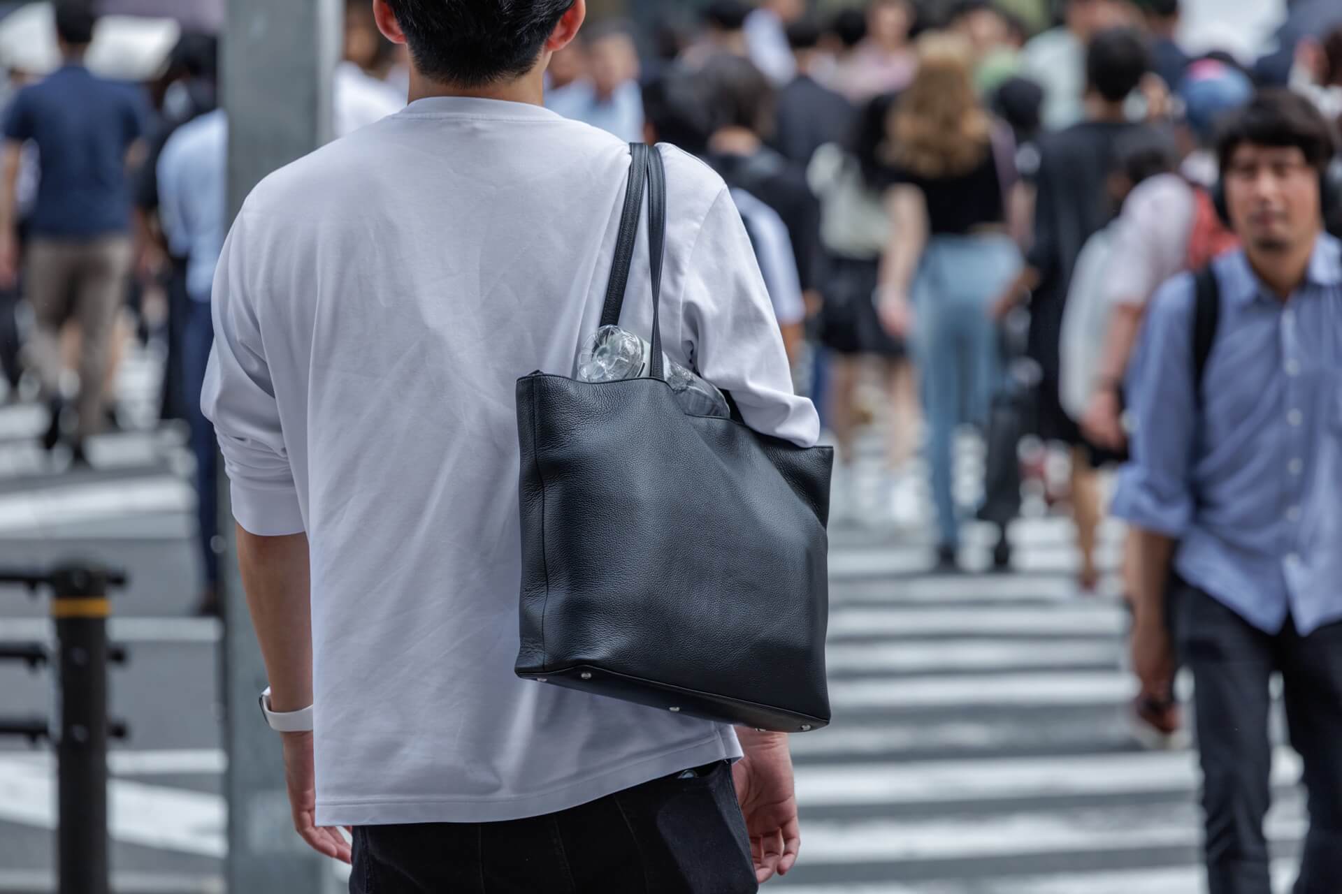 黒いレザーのトートバッグを肩にかけて街を歩く男性