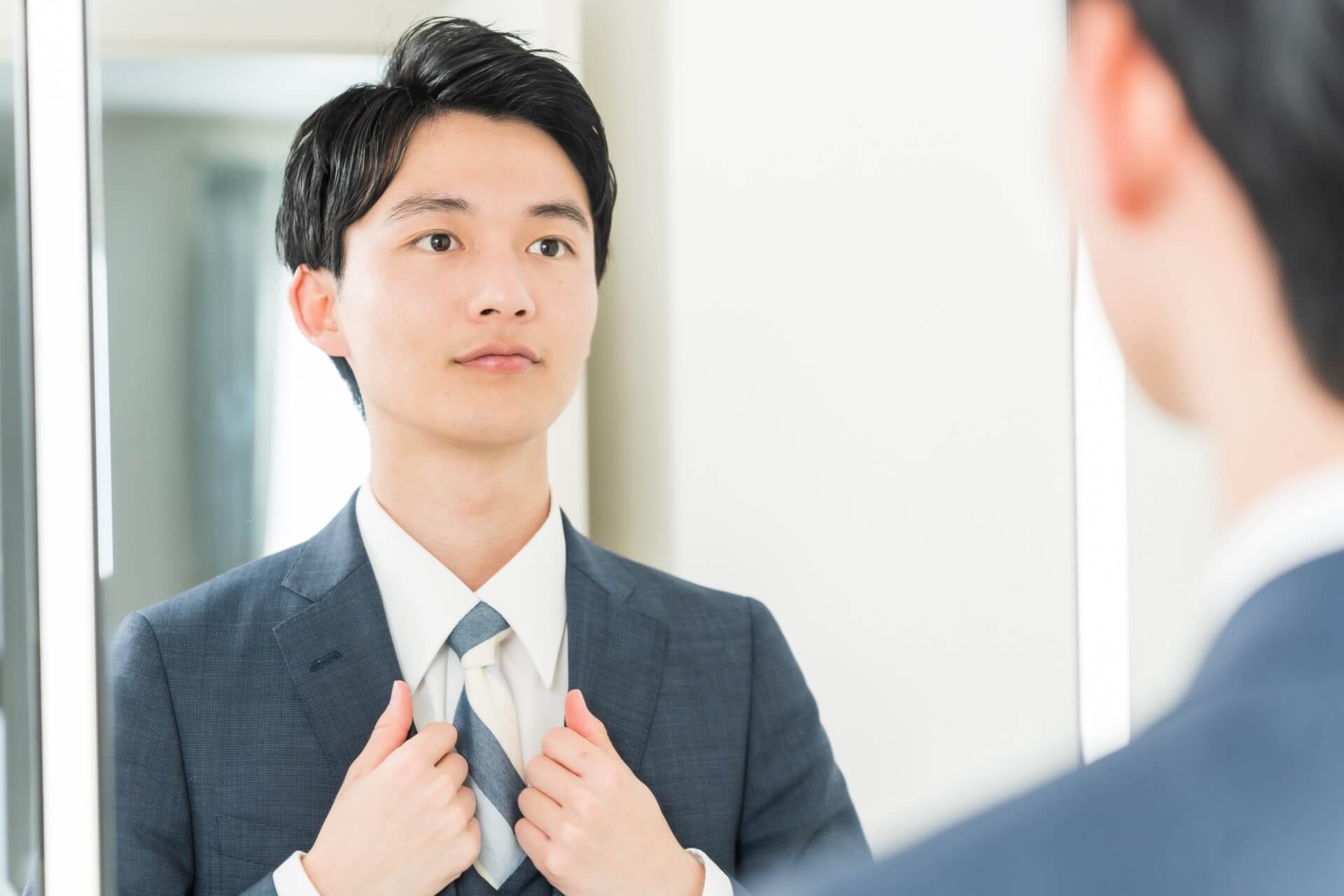 スーツ姿で鏡に向かい身だしなみを整える男性