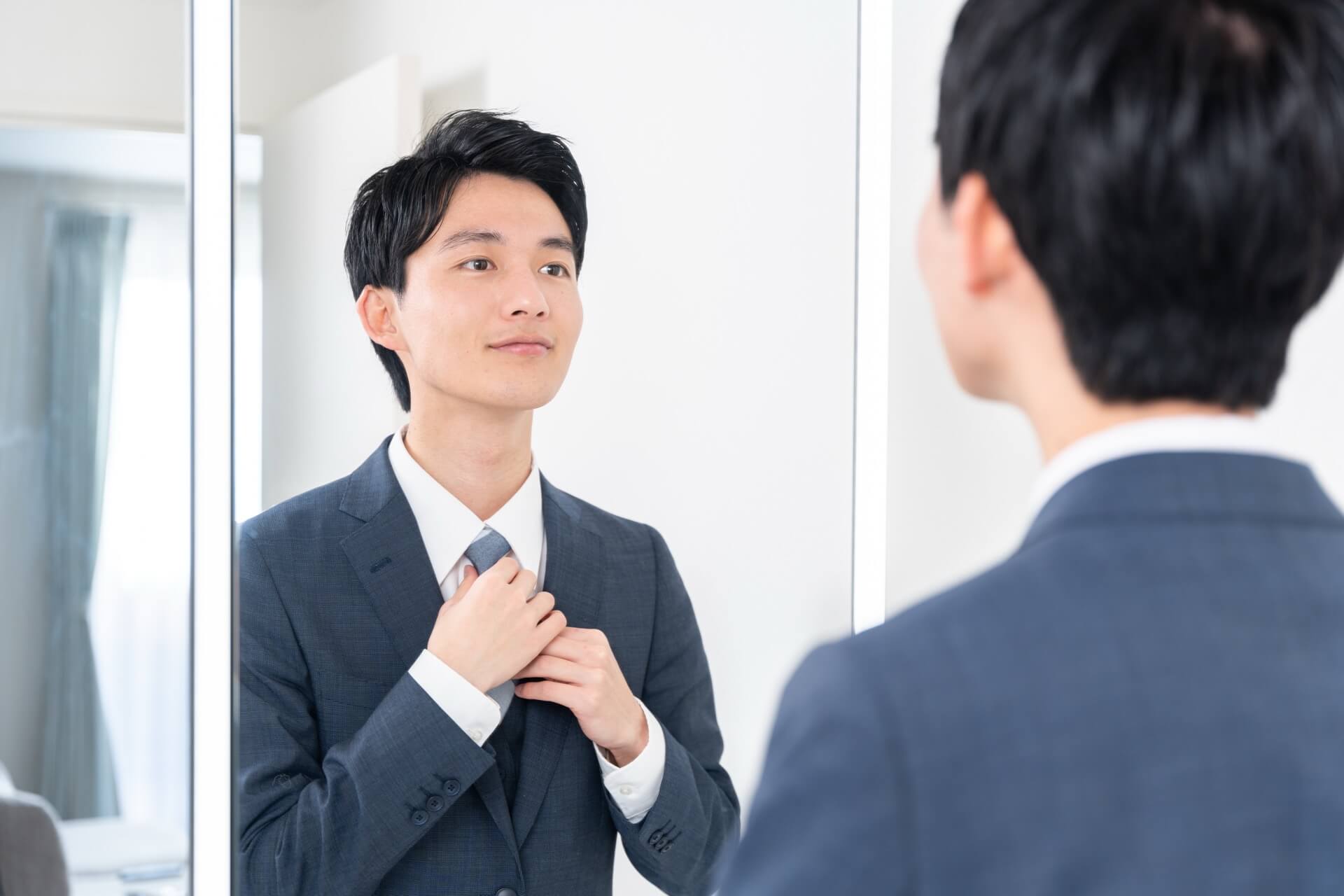 鏡を見ながらネクタイを締めるスーツ姿の男性