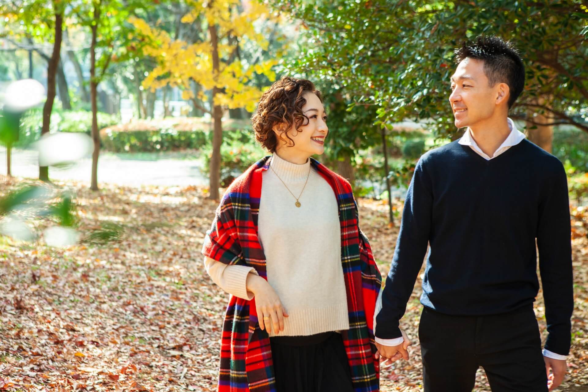 紅葉の公園を並んで歩きながら笑顔で話す大人の男女