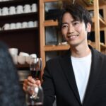 ジャケットに白いカットソーを合わせ、グラスを手に笑顔で話す男性