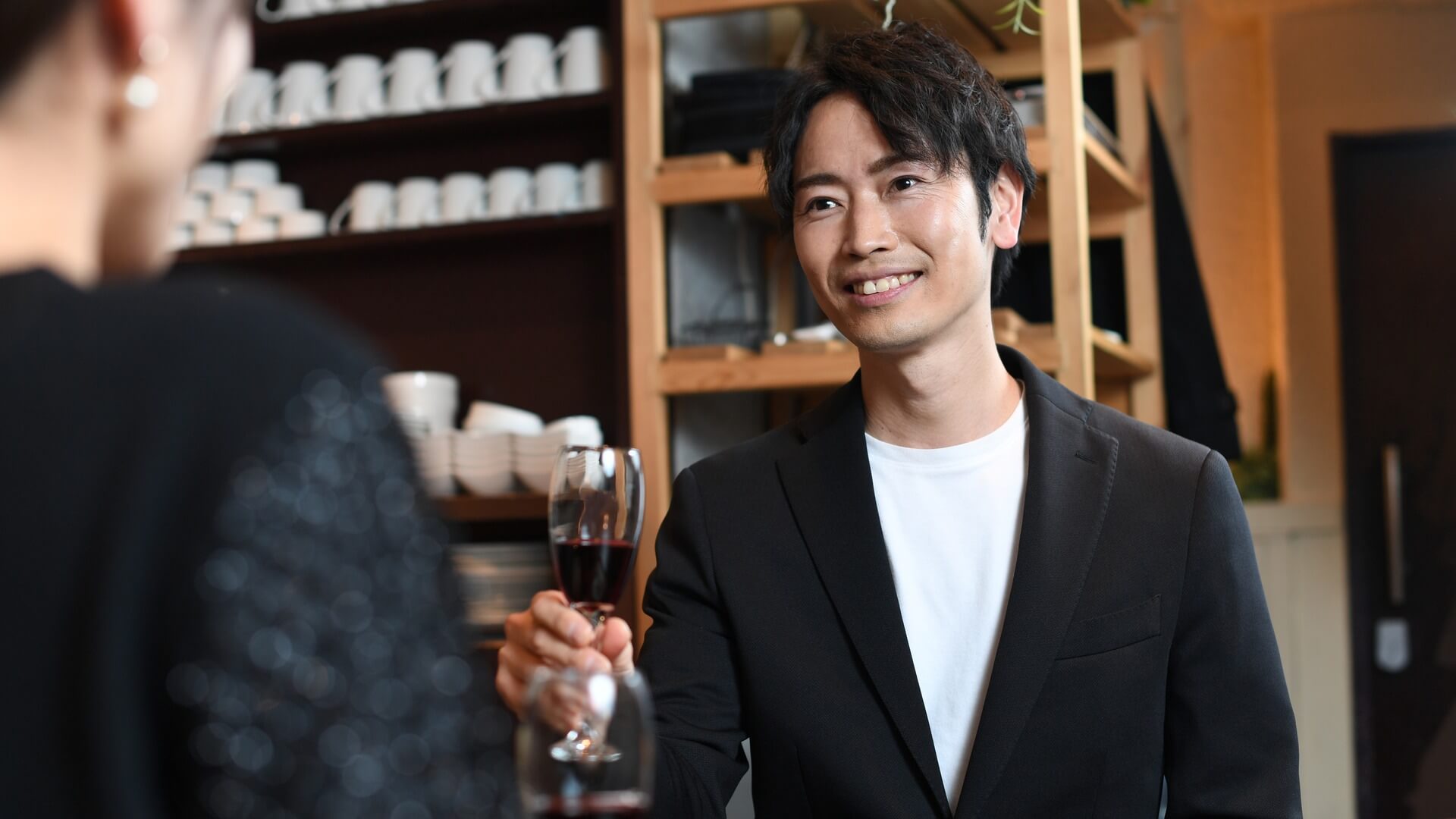 ジャケットに白いカットソーを合わせ、グラスを手に笑顔で話す男性