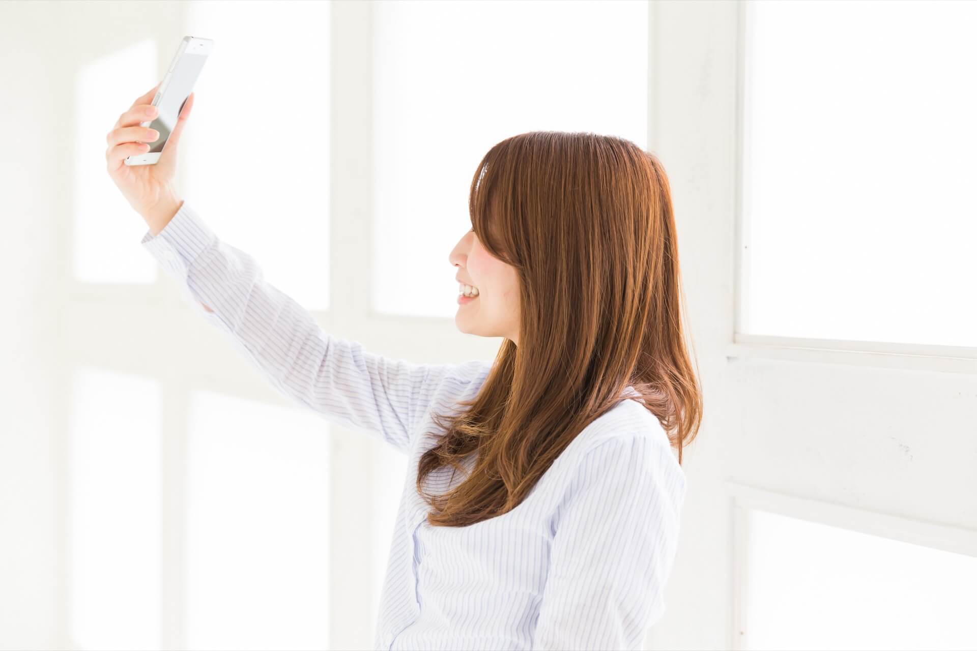 窓際でスマートフォンを掲げて自撮りをする女性