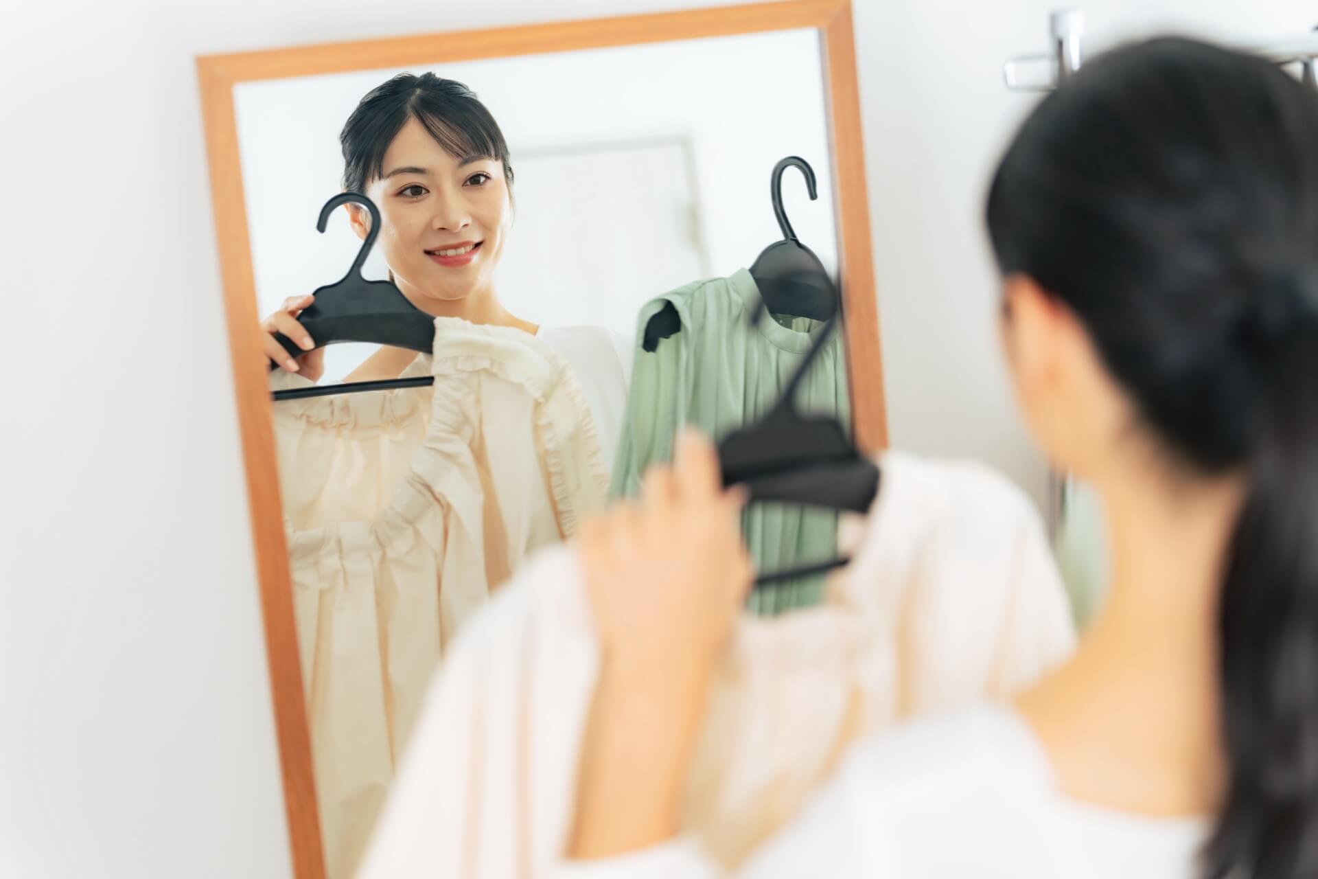 鏡の前でワンピースを2着手に取り、どちらを着るか見比べる女性