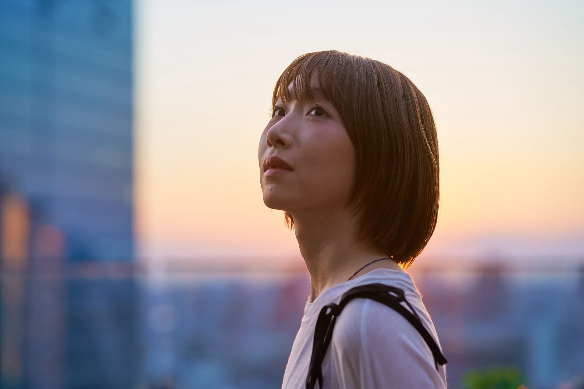 夕暮れの街で空を見上げて考えごとをする女性