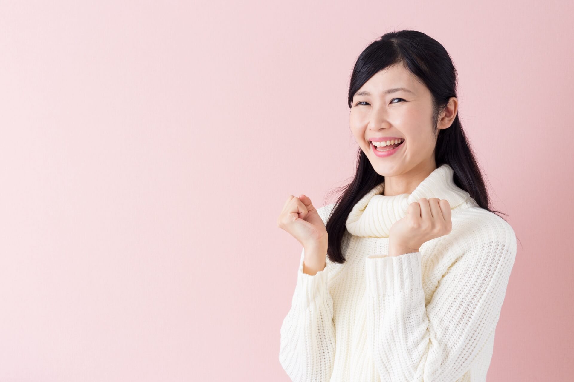 ピンクの背景で白いタートルネックのニットを着て笑う女性