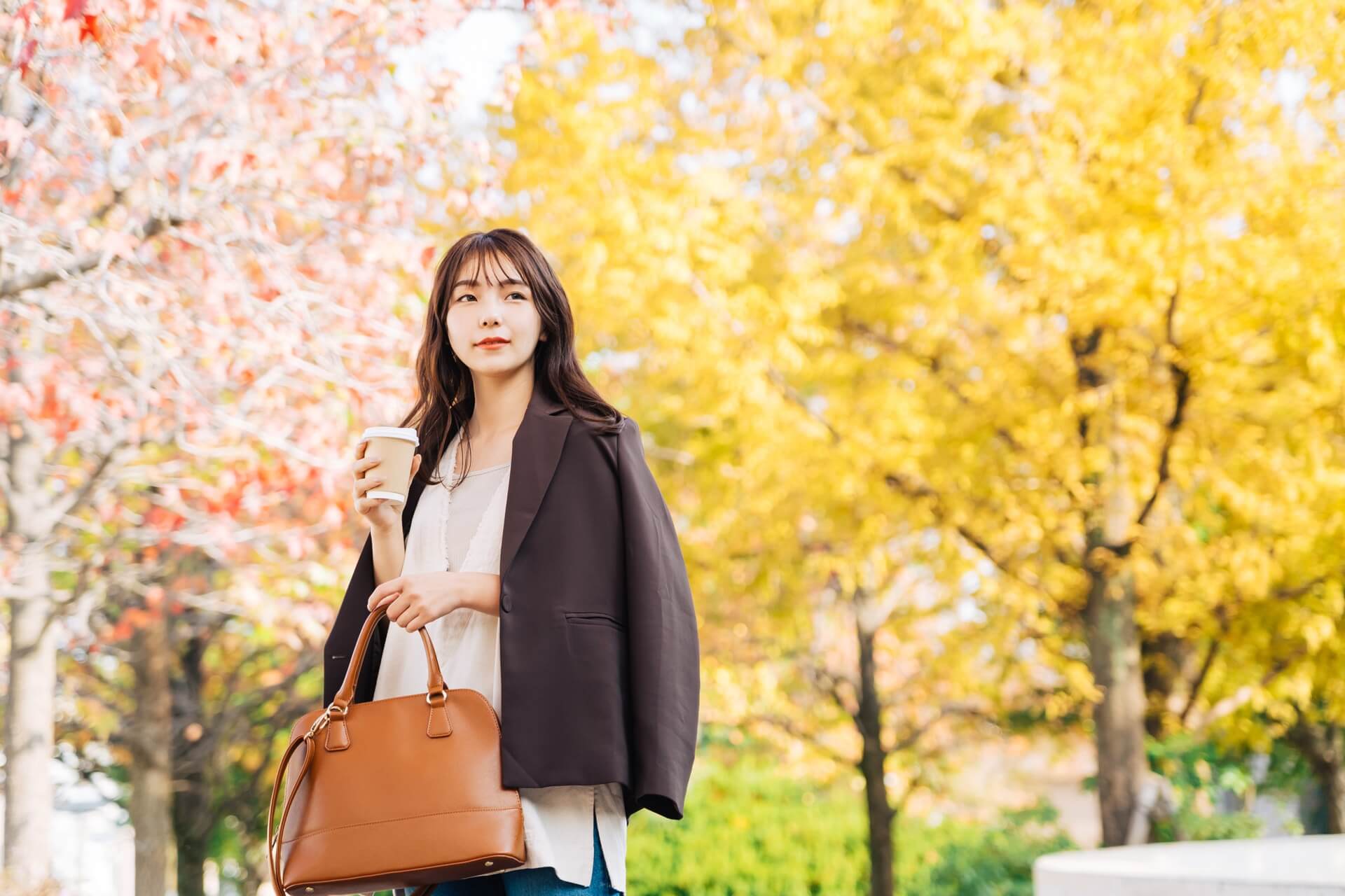 紅葉した街でジャケットを羽織りバッグを持つ女性