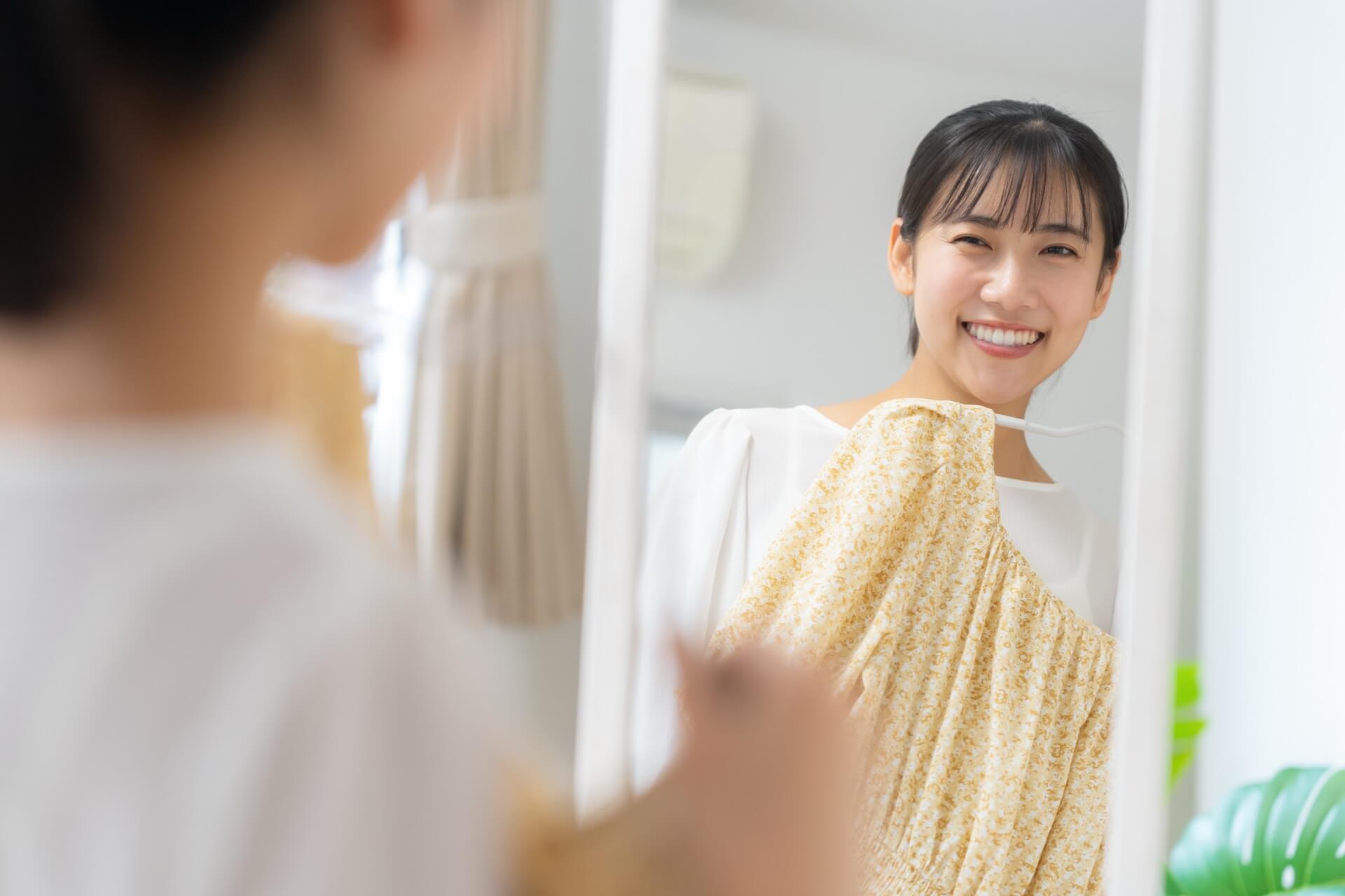 鏡の前でワンピースを体に当てて服を選ぶ女性