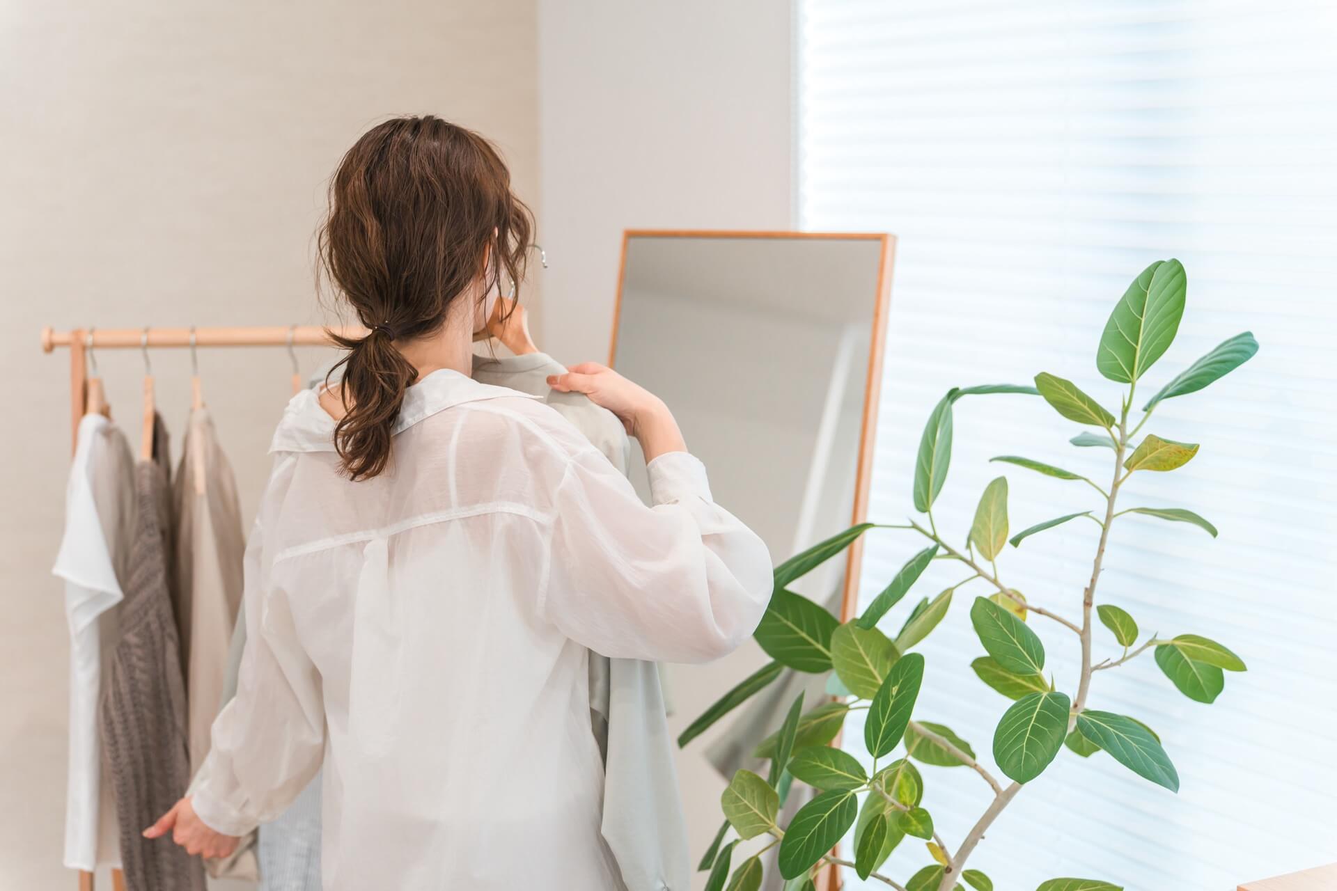 鏡の前でハンガーの服を体に当ててデート服を選ぶ女性