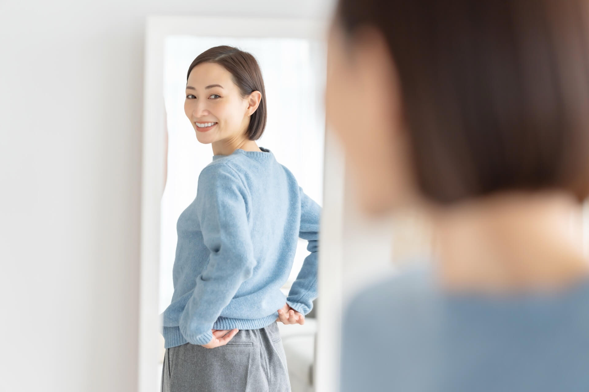 ニットを着て、姿見で服の見え方を確かめる女性