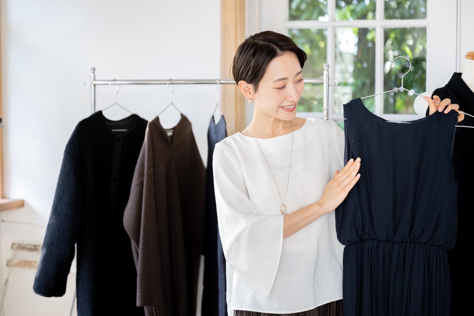 白いブラウスの女性がネイビーのワンピースを手に取って選んでいる様子